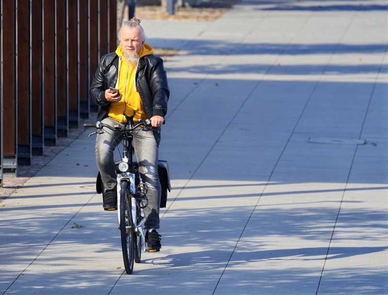 11 - A man with a gray beard and hair bun is riding a utility bicycle while looking at his smartphone